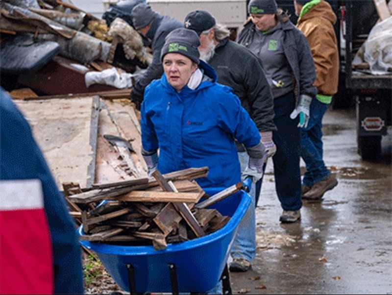 UMCOR worker pushing wheelbarrow full of debris